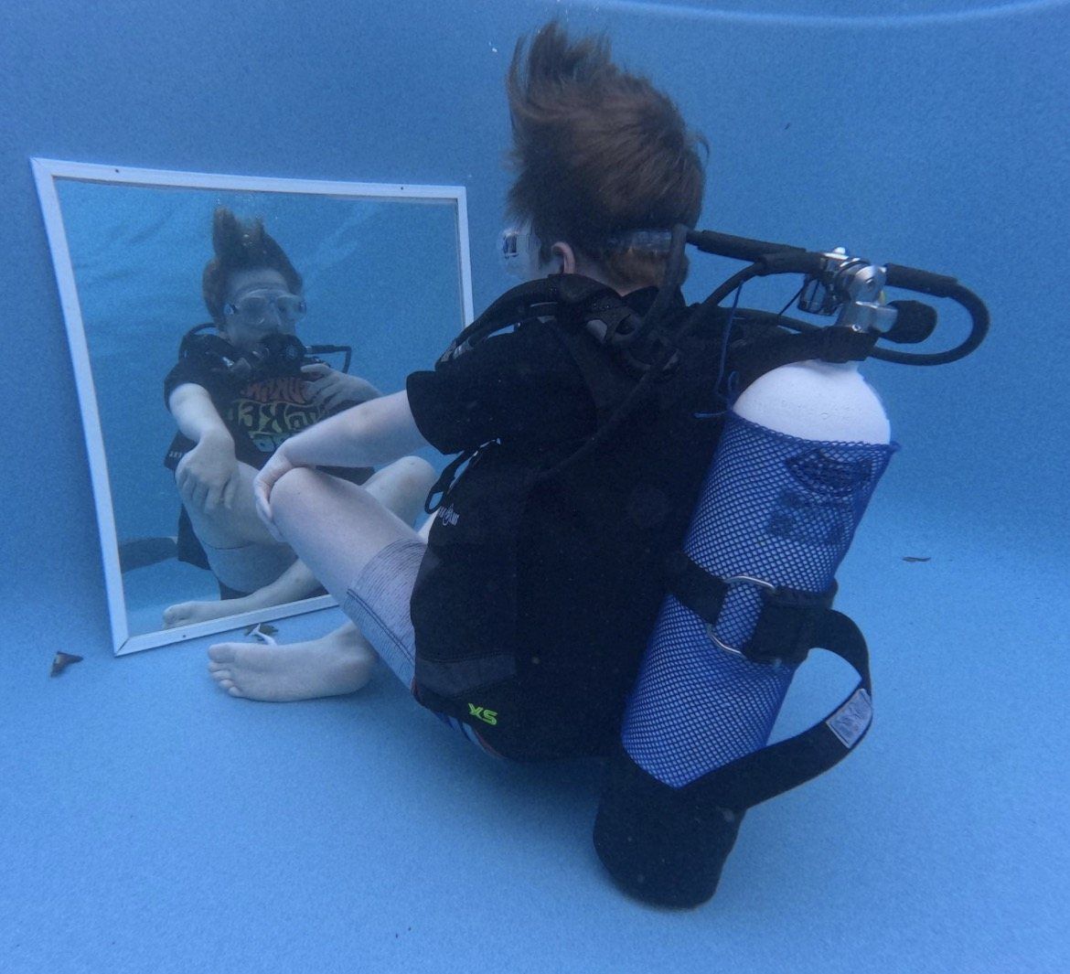 One person in scuba gear sitting calmly on the floor of a pool